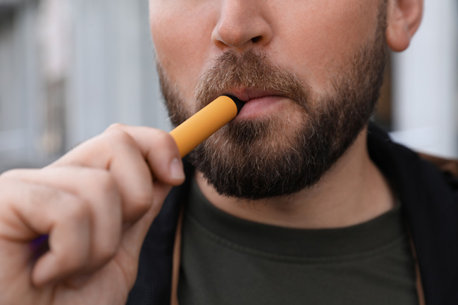 A man holds a disposable vape to his lips.