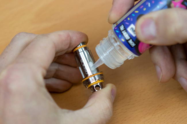 Image of a hand holding a vape coil and priming it with a vape juice bottle