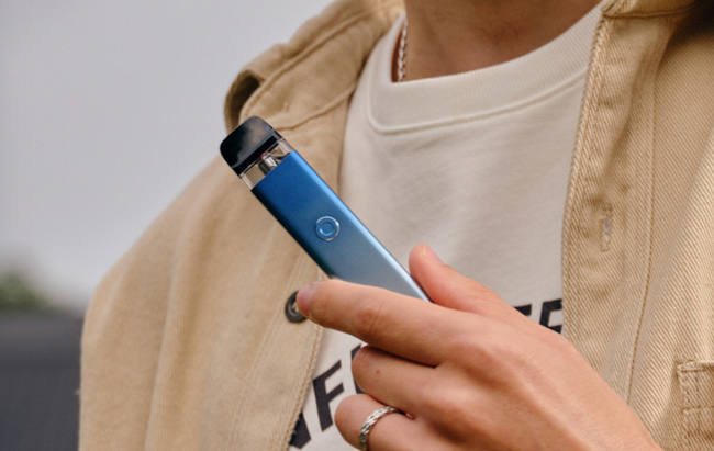 A ringed finger holds a blue Vaporesso Xros 3 device.