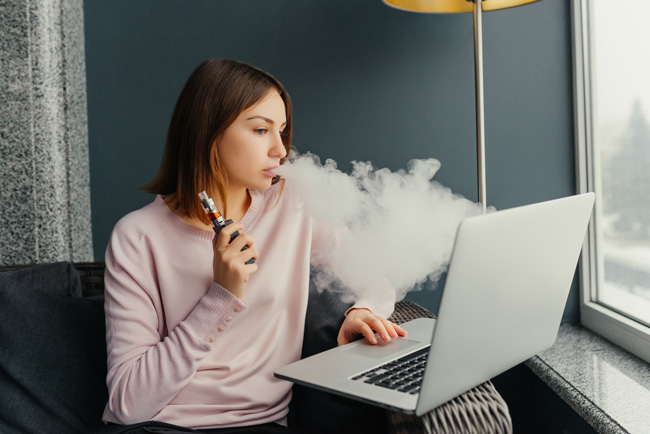 A woman vapes while doing research on a macbook pro.