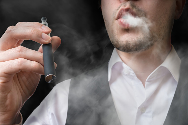 Man pictured from nose down exhales vapour while holding an old device in his hand.