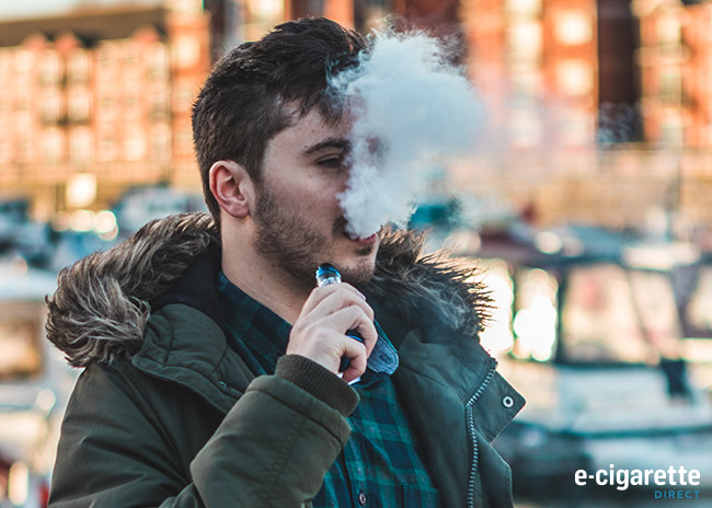 A man holding a vape device with a large cloud of vapour coming from his mouth