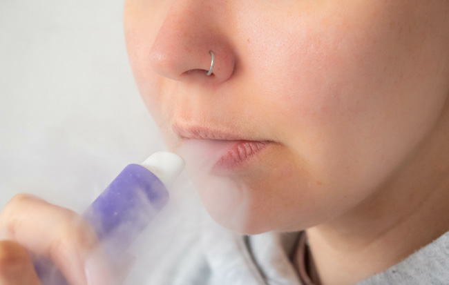 A person holding a disposable and exhaling vapour