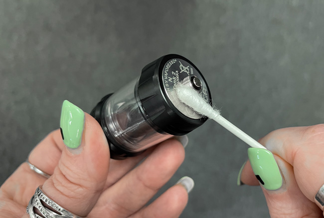 A hand cleaning the base of a vape tank with a cotton bud.
