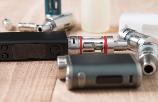A selection of vape mods and tanks on a wooden table surface.