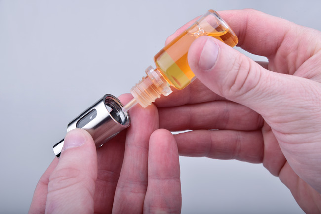 A hand holding an e-liquid bottle and priming a coil