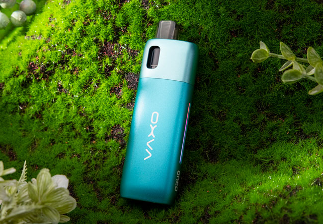 Blue Oxva Oneo vape device surrounded by greenery.
