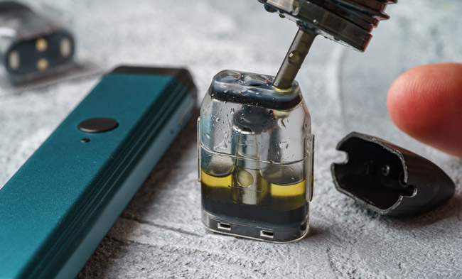 A vape device's pod being filled with e-liquid.