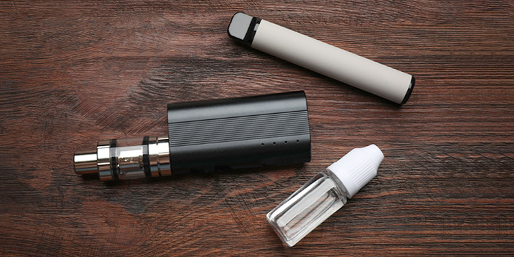 Image of 2 vape devices and 1 vape juice bottle on a wooden table