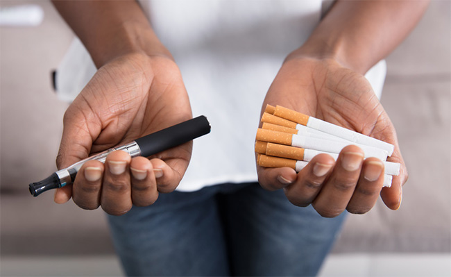 Hands holding a vape and cigarettes.